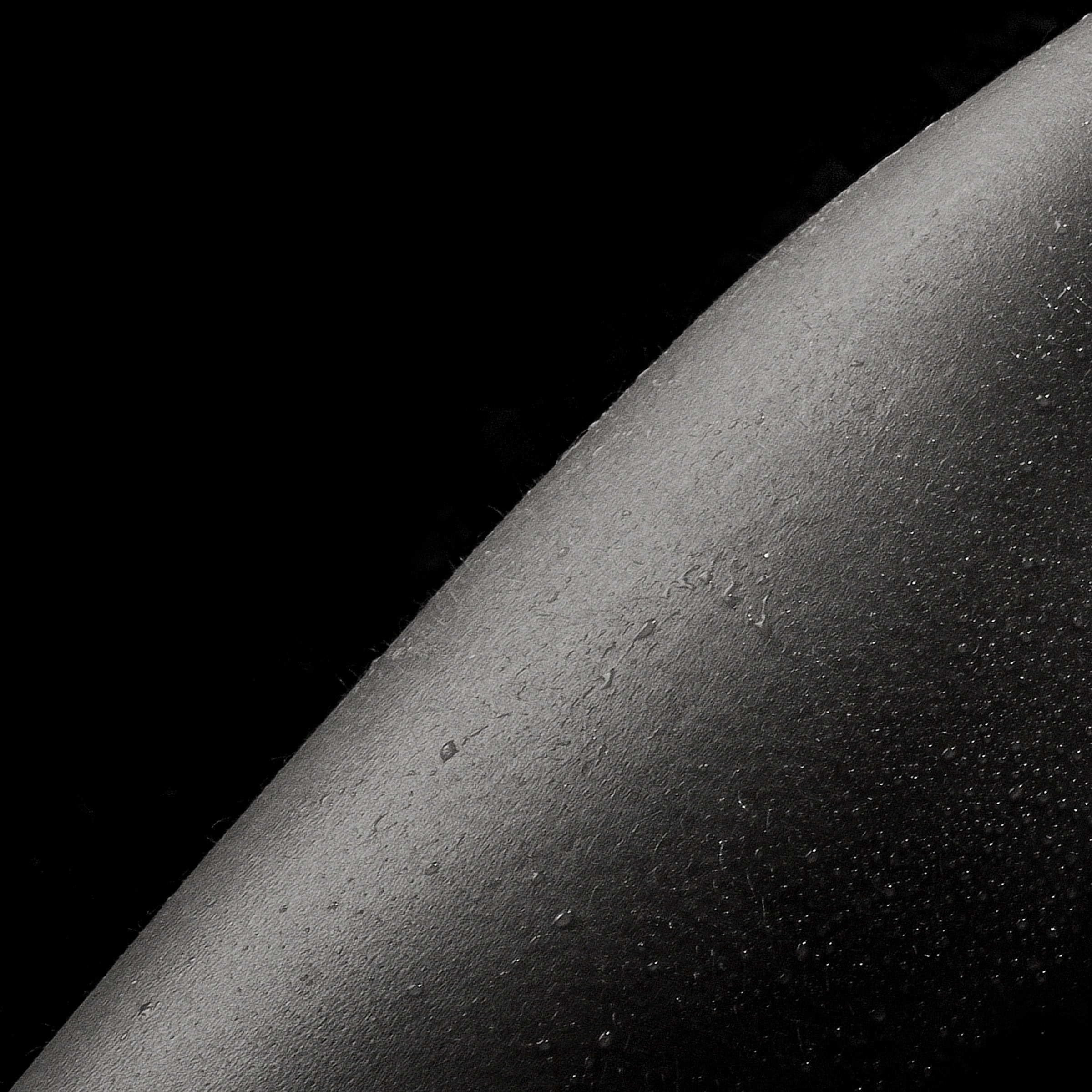 Curve of a lit body against black, water on skin