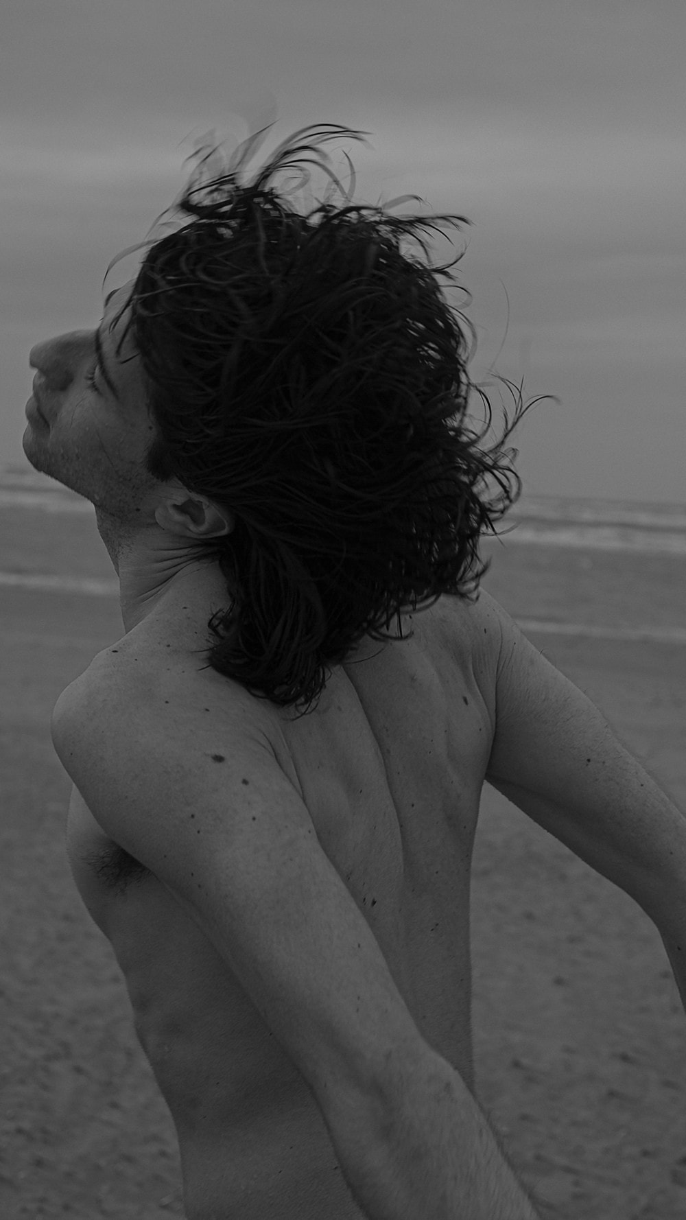 From behind: bare back and shoulder blades, head flung back in profile with wet hair flying at dusk.