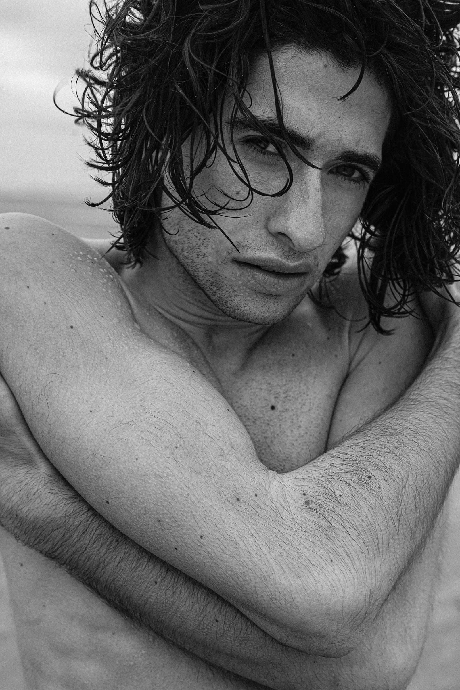Tight portrait, bare shoulders and one arm crossed over his chest, wet curls, a direct and unguarded look at the camera.